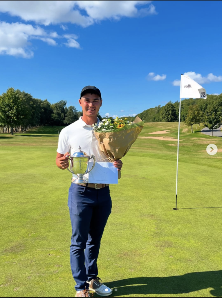 Oliver Bredahl-Kjær med pokal og blomster på golfbanen.
