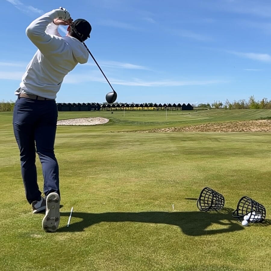 Golfspiller slår bolde på driving range med en kurv med golfbolde ved siden af
