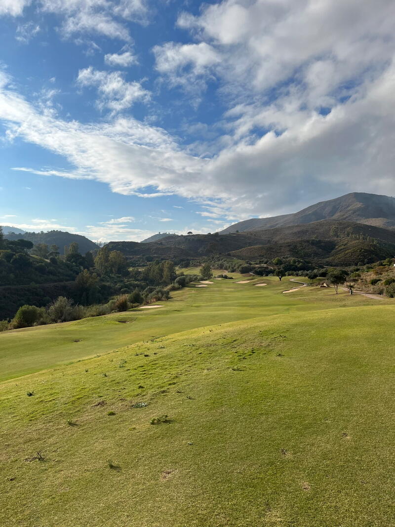 Fairway med bjerge og skyer i baggrunden