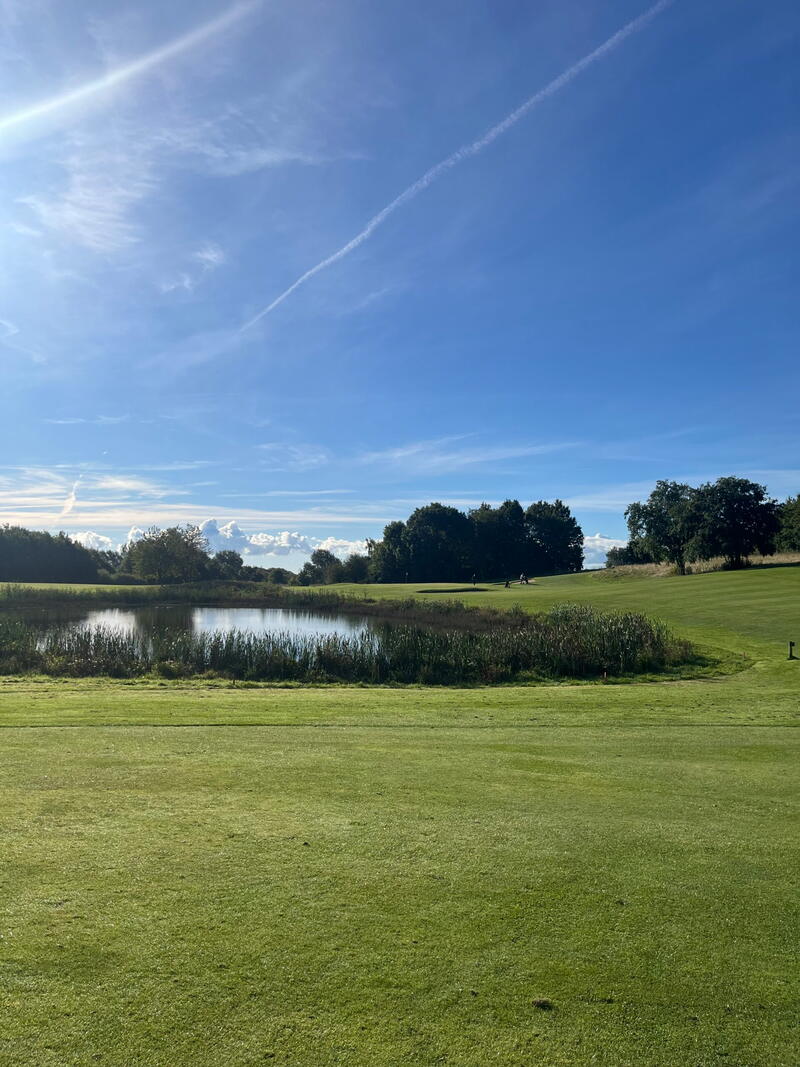 Fairway med en sø i baggrunden under blå himmel med tynde skyer