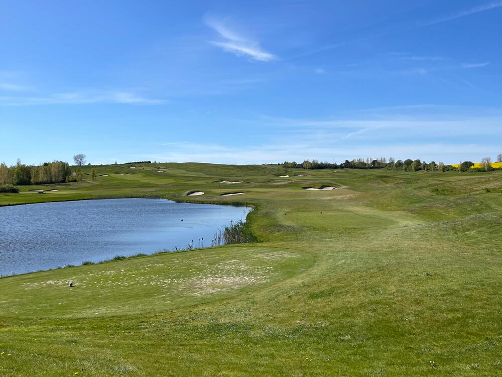 Solrig golfbane med sø og golfbunkere i baggrunden